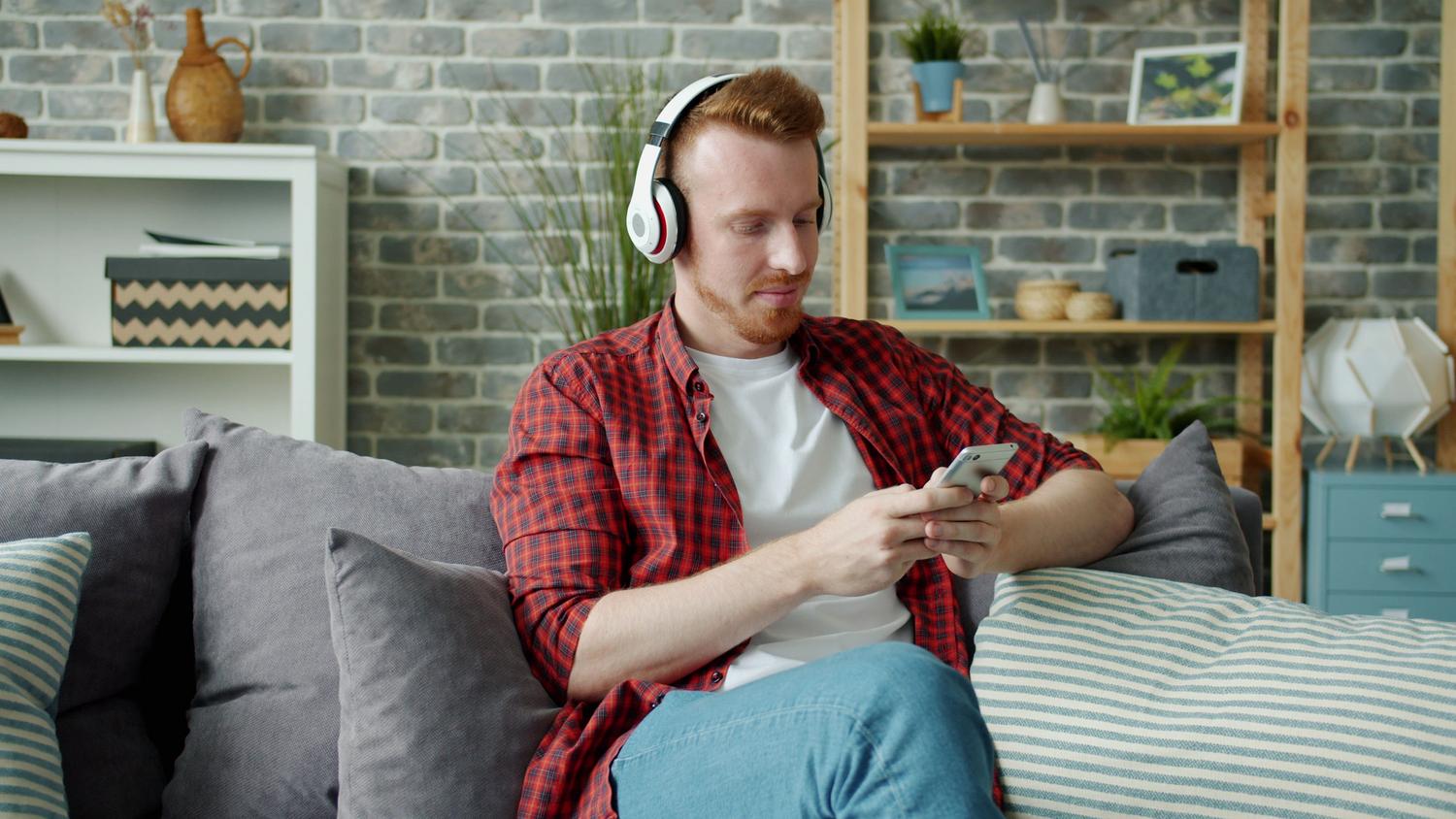 Hombre relajado en un sofá utilizando auriculares inalámbricos y un smartphone, mostrando la experiencia de uso cotidiano.
