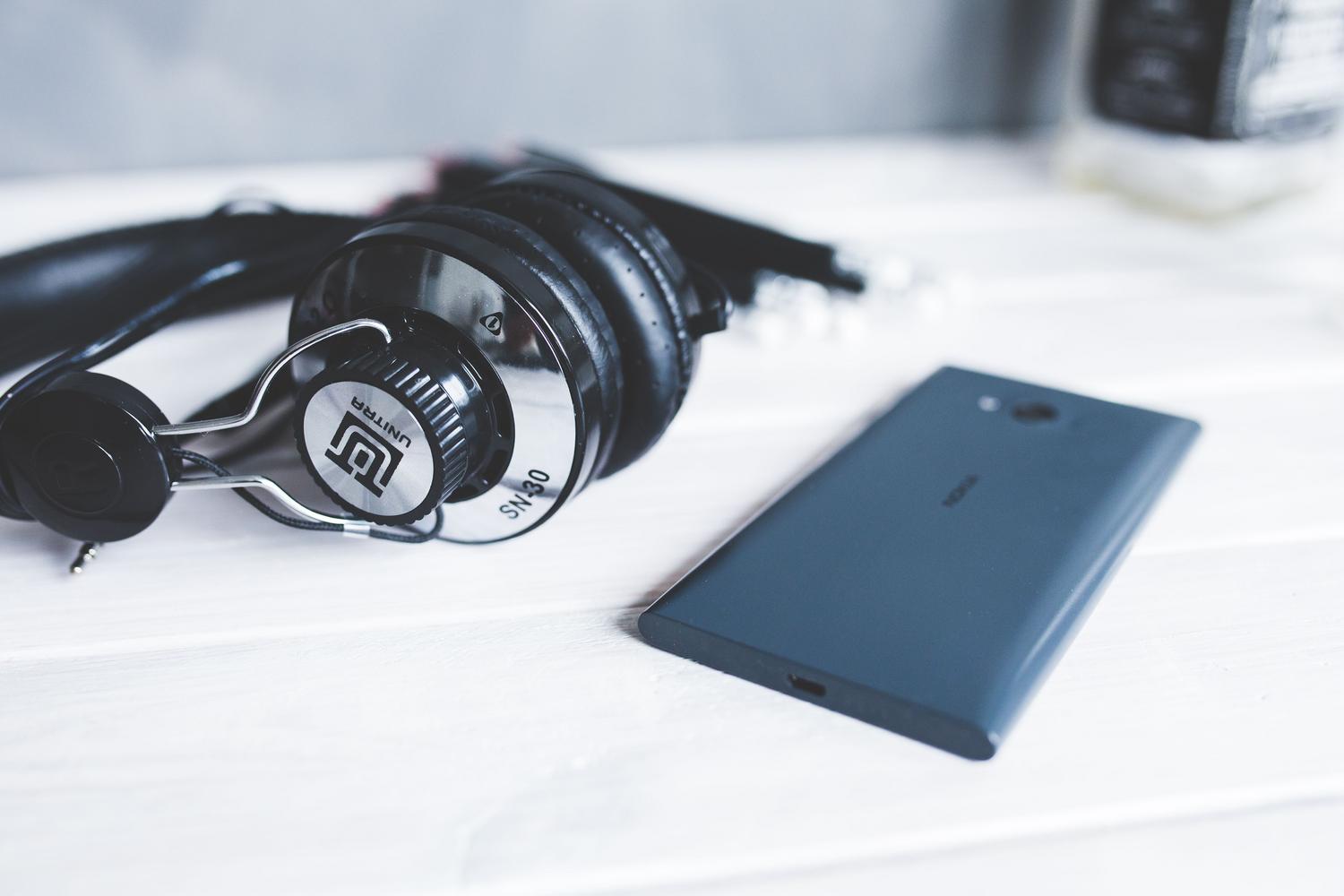 Auriculares negros y un teléfono inteligente sobre una mesa de madera, una imagen limpia y minimalista sobre música digital.